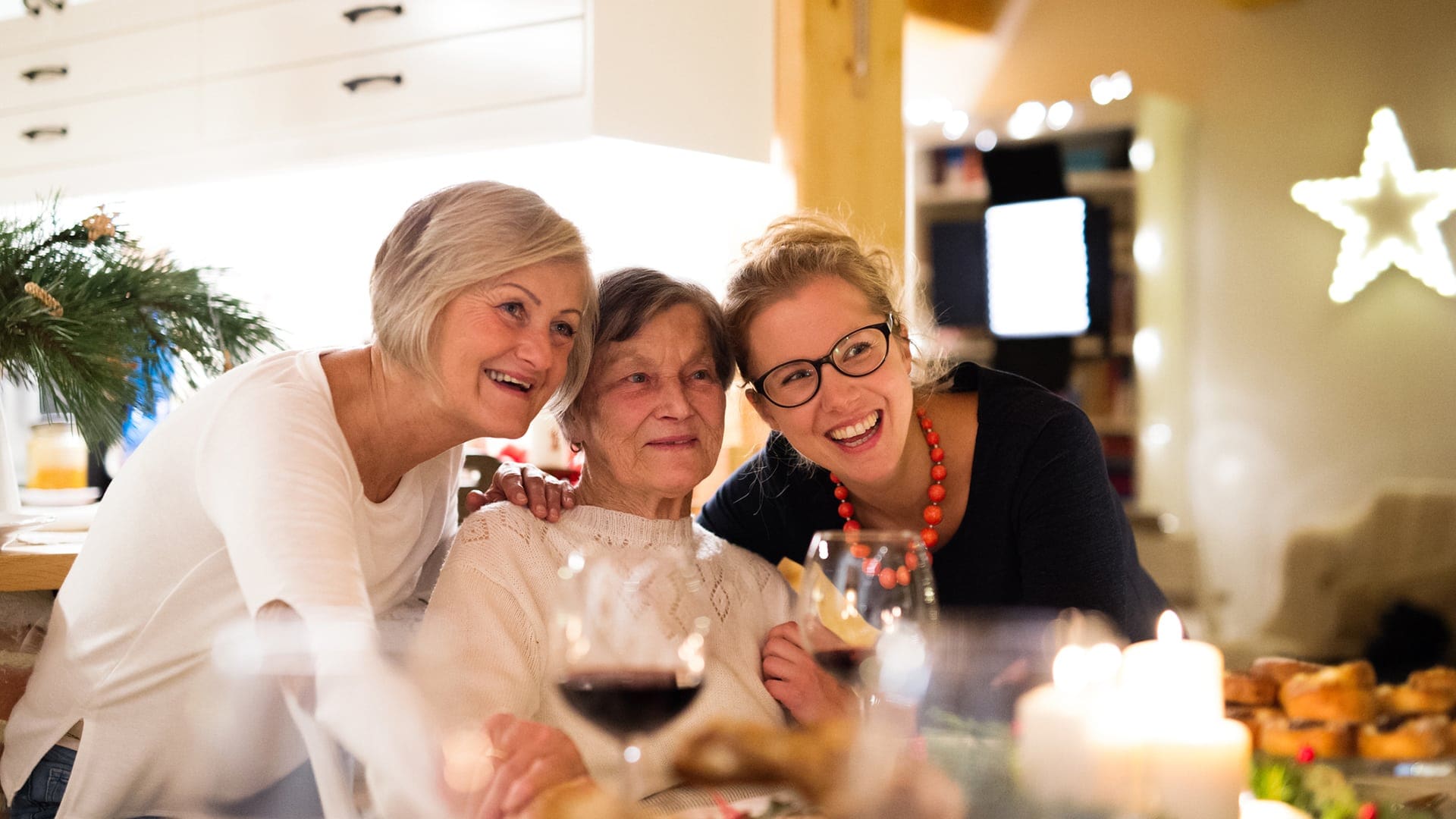 Three generations of smiling women enjoying quality time together around a warmly lit dining table.