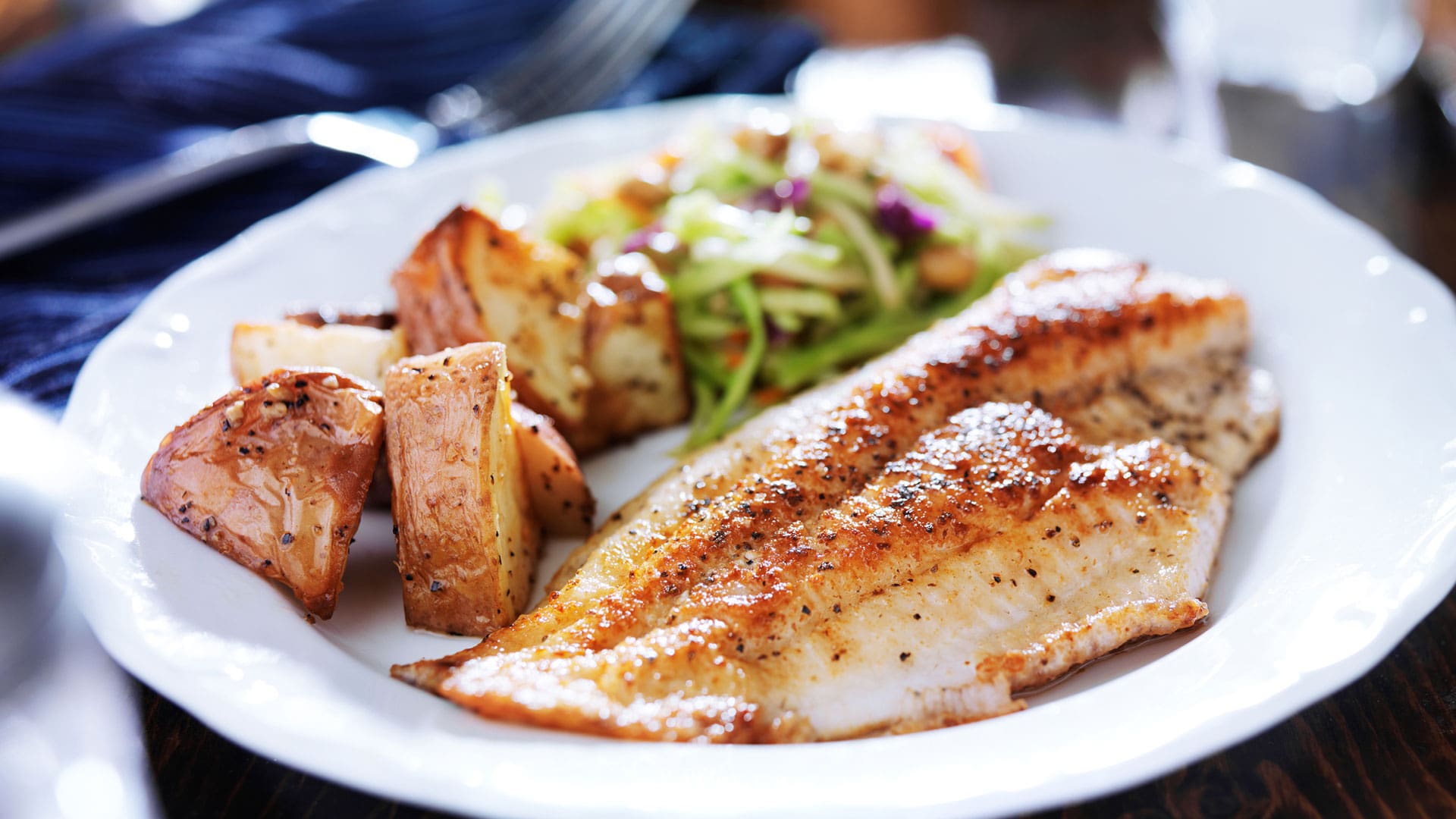 Plate featuring a healthy and visually appealing meal of grilled fish, roasted potatoes, and fresh salad.
